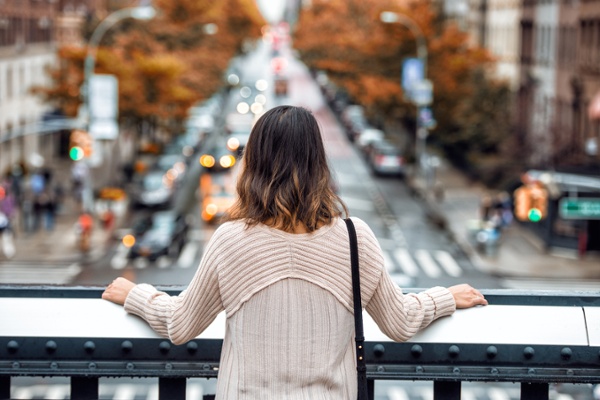 woman leaning against a bridge railing and looking at a downtown intersection without pest birds